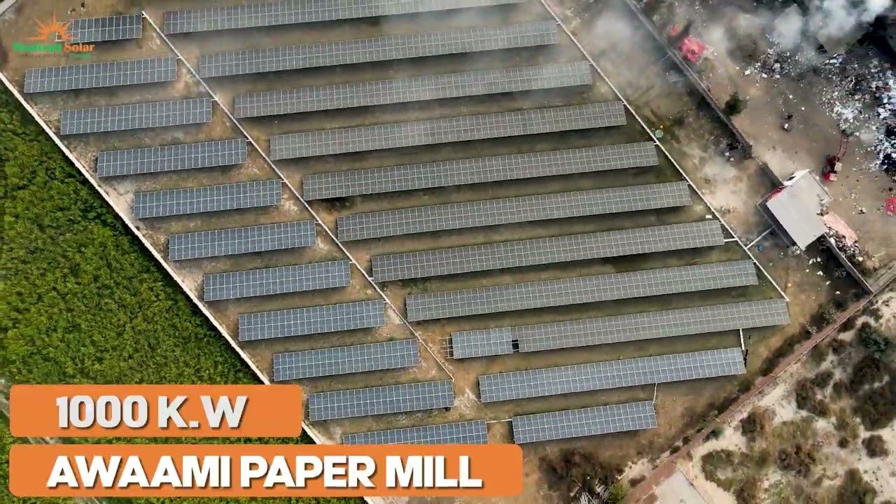 Aerial view of a ground-mounted solar array beside the buildings of a paper mill in Faisalabad